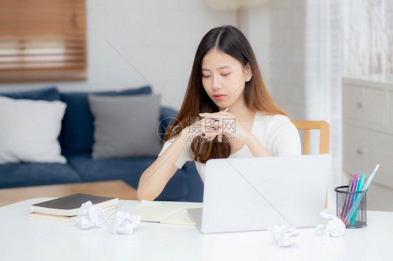 年轻的亚洲女在家里用笔记本电脑思考创意项目和纸张在桌子上有问题女孩在用笔记本电脑时有挫败和麻烦商业和自由职业者的概念图片