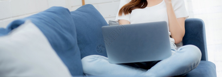 面对戴具的年轻亚洲商业妇女透过笔记本电脑到客厅的互联网上工作图片
