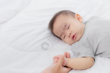 年轻的幼母亲触摸着小女婴的手在卧室床上温柔地躺在母亲爱新生儿和护理妇女与子父母和儿一起表达家庭概念图片