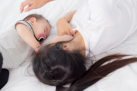 年轻的幼母亲触摸在卧室床上温柔地躺在的小女婴头部母亲爱新生儿和护理妇女与子父母和儿一起表达家庭概念图片