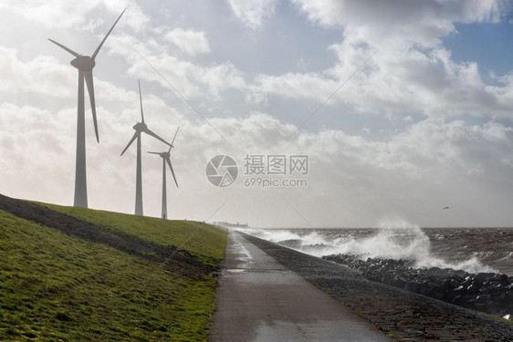 荷兰海岸有风力涡轮机可以看到乌尔克村的天际线暴风雨的海浪正在海岸上拍打荷兰海岸有风力涡轮机在暴风雨中破浪前进图片