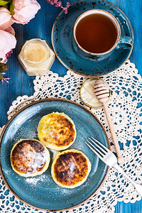 蓝背景的古董杯中含奶油和茶叶的椰子奶酪煎饼蜂蜜和茶叶图片