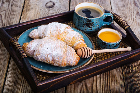 羊角面包蜂蜜和浓缩咖啡放在木制托盘上的蓝色老式碗里摄影棚照片羊角面包蜂蜜和浓缩咖啡放在木制的蓝色老式碗里图片