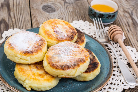 早餐俄罗斯传统干酪煎饼糖粉和蜂蜜放在一块旧木制桌板上图片