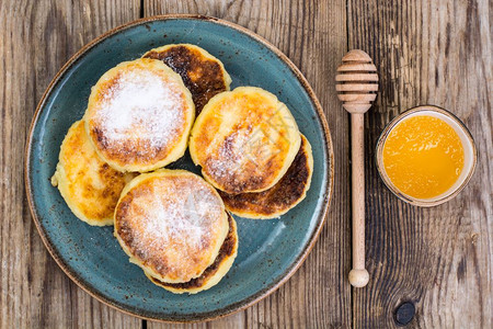 蜂蜜早餐早餐俄罗斯传统干酪煎饼糖粉和蜂蜜放在一块旧木制桌板上背景