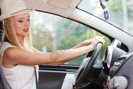 漂亮的女人坐在车里室内的车轮上笑着漂亮的金发女郎准备在假期旅行图片