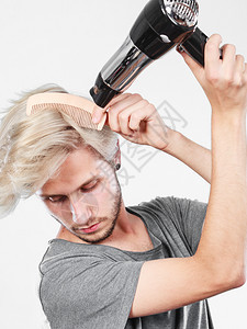 发型和时尚年轻时尚的男理发师有着改变发型的新想法金发男人拿着吹风机和梳子做新发型年轻人用吹风机吹风图片