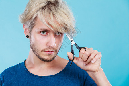 发型和发型年轻帅哥手里拿着理发师的专用剪子工具就在蓝色男人用剪刀织纹或变薄剪刀背景图片