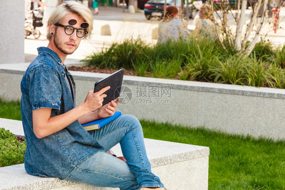 男时尚科技学生观念一个穿着牛仔裤戴着古怪太阳镜坐在白色窗台上的家伙坐在窗台上拿着平板电脑的时髦男人图片