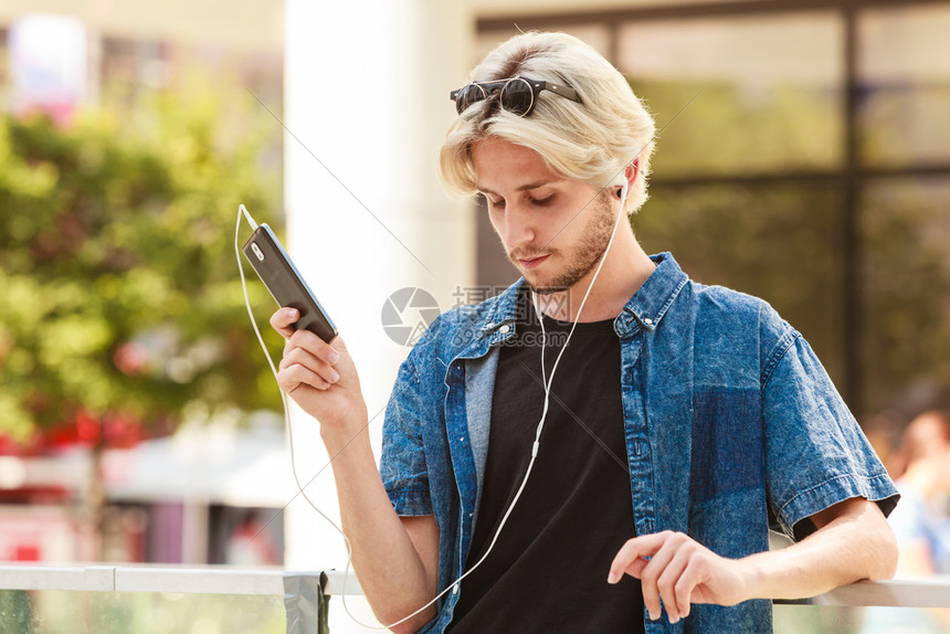 男子时装技术城市风格服装概念穿着牛仔服站在城市街道上的人穿牛仔服通过耳机监听音乐男子时装城市风格服概念穿牛仔服站在城市街道上的人图片