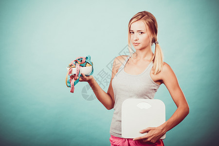 饮食健康饮食瘦身理念健身女孩拿着碗碗里有许多彩色的卷尺作为节食的标志和体重秤工作室拍摄于蓝色图片