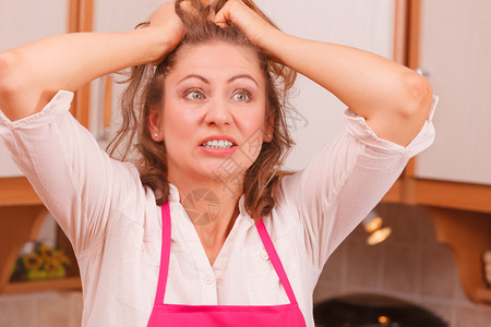 穿着粉色围裙的惊慌和忧心忡的女人厨房焦虑和紧张家庭主妇消极的面部情绪厨房的悲伤家庭主妇背景图片