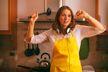 在家厨房做饭和穿着耳机的可爱家庭主妇用勺子拉跳舞在室内厨房跳舞的家庭主妇图片