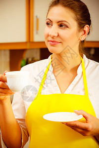 围裙上的成熟女在厨房里端着一杯咖啡家庭主妇有热能饮料咖啡因量在厨房里端着一杯咖啡图片
