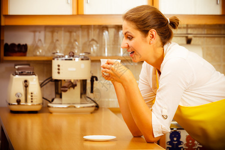 坐在围裙上的成熟女在厨房里端着咖啡杯家庭主妇有热能饮料咖啡因成熟女在厨房里端着咖啡杯成熟女在厨房里端着咖啡图片