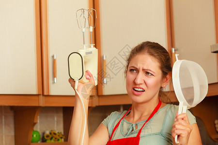 手拿着搅拌机的女主妇和头部筛子训练员围裙上的成熟女人在厨房玩得开心图片