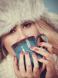 时装概念冬的金发女人喝杯茶热饮蓝背景黄发女人冬的金毛帽子喝酒图片