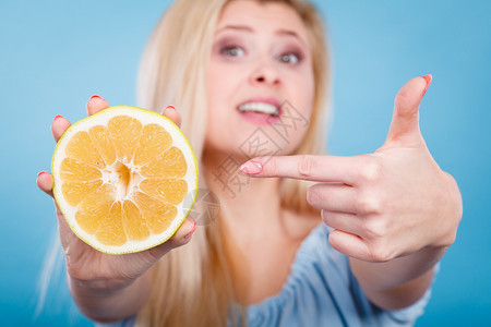 怀着一半绿色黄葡萄果柑橘水用手指着建议健康饮食在蓝色上微笑的女孩图片