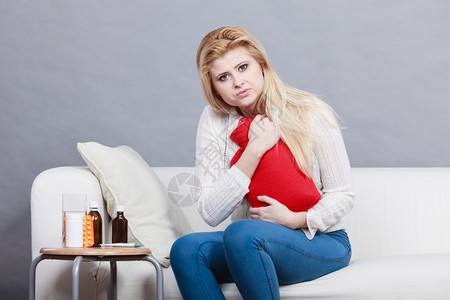 胃痛期和月经抽筋问题概念在可口上坐着肚子抽筋的妇女感觉非常不舒服用热水瓶来感到宽慰在可口乐上坐着肚子抽筋图片