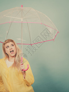 穿着黄色雨衣的金发女子带着透明的雨伞观察天气图片