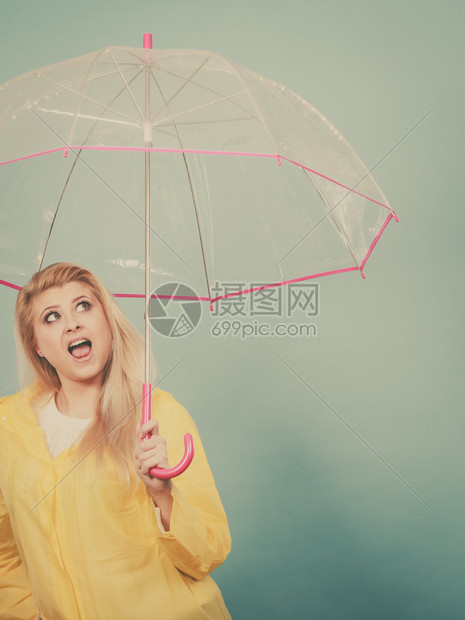 穿着黄色雨衣的金发女子带着透明的雨伞观察天气图片