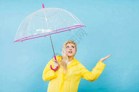 身穿黄色雨衣的金发女人拿着透明的雨伞检查天气是否下雨图片