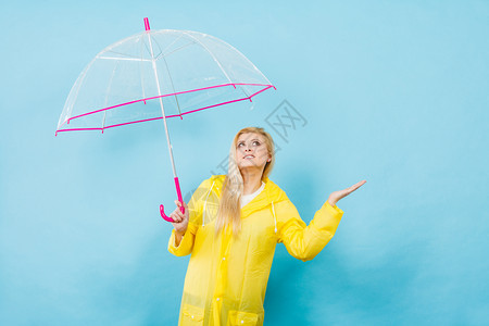 身穿黄色雨衣的金发女人拿着透明的雨伞检查天气是否下雨图片