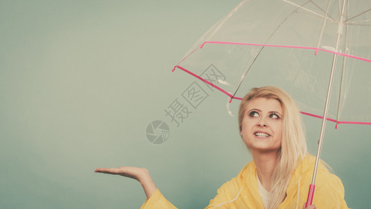 身穿黄色雨衣的金发女人拿着透明的雨伞检查天气是否下雨图片