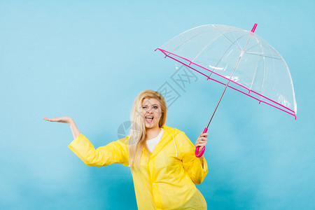 身穿黄色雨衣的金发女人拿着透明的雨伞检查天气是否下雨图片