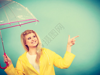 身穿黄色雨衣的金发女人拿着透明的雨伞检查天气是否下雨图片