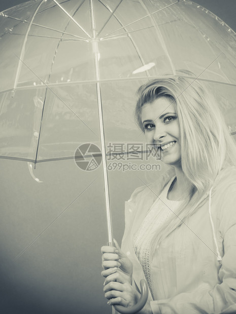 雨天时心情良好金发妇女快乐穿着雨衣拿透明伞戴图片