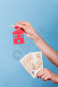 家庭储蓄和财政经济概念持有钱和房钥匙的人蓝背景摄影棚拍图片