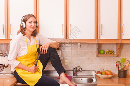 在厨房里放松听音乐有趣的快家庭主妇做厨师耳机戴着黄色围裙坐在家里放松图片