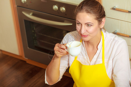 在厨房喝咖啡的围裙上成熟女人家庭主妇休息在地板上时放松在厨房喝咖啡的成熟女人图片