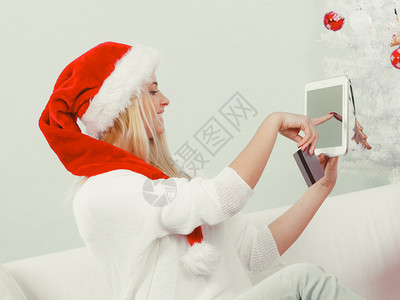 圣诞节时间概念年轻女少有平板电脑笔记本和信用卡的年轻女孩在家沙发上做网购物买浏览礼品玩乐有平板信用卡的女孩在网上购物图片