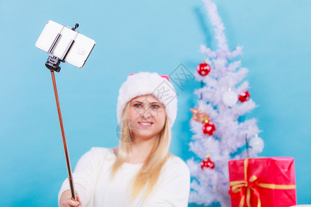 现代假日概念穿着圣诞礼帽的金发女人给自己拍圣诞照手持智能机的自拍背景图片