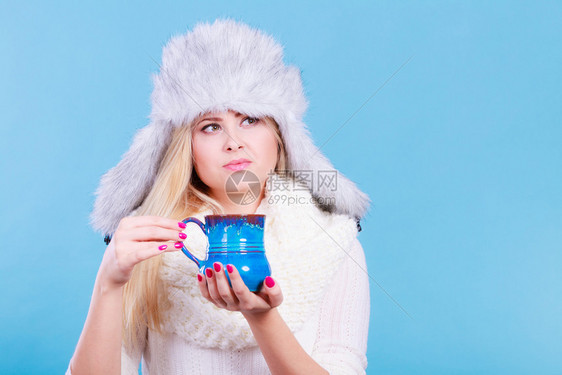时装概念寒冷穿衣服的套件和穿着俄罗斯风格的冬衣金发女郎温暖的毛帽和用杯子喝热饮料的围巾戴冬帽的女子喝杯图片