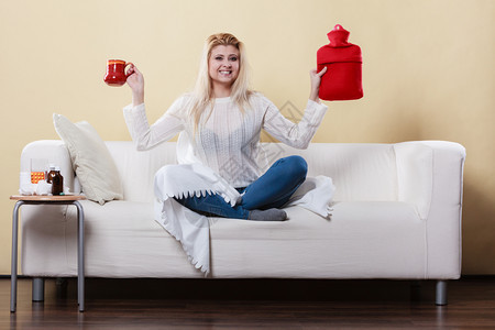 快乐的女士展示了摆脱热水瓶和喝的发烧方法坐在杯子上沙发放松图片