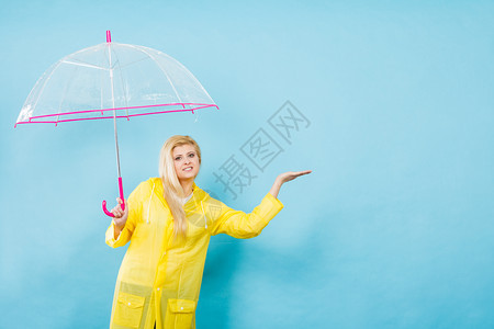 身穿黄色雨衣的金发女人拿着透明的雨伞检查天气是否下雨图片