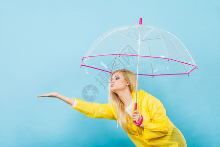 身穿黄色雨衣的金发女人拿着透明的雨伞检查天气是否下雨图片