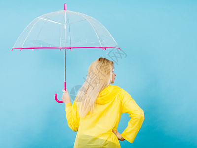 穿着雨衣的金发妇女持透明伞背视图片
