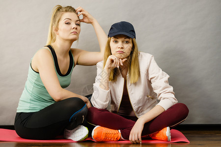 两个穿着运动服的有吸引力妇女坐在运动垫子上艰苦的锻炼后感到无聊或疲劳图片