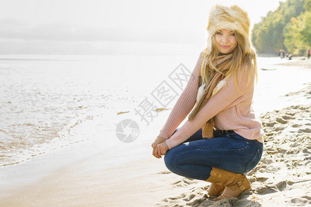 年轻女在秋天的气下海滩户外度过时间穿着毛衣蓝色牛仔裤和毛帽图片