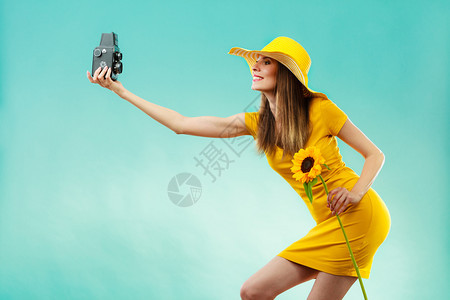 身着黄色洋装和向日葵帽子的暑期妇女穿着黄色洋装戴向日葵帽用蓝背景的旧照相机自拍图片