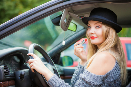 年轻有吸引力的女士在驾驶汽车时用化妆品涂上唇膏图片