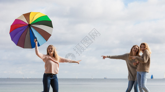 带着五颜六色雨伞的女人她的两个朋友在取笑她取笑她女人取笑跳朋友图片