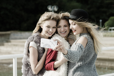 三位女自拍在户外用智能手机拍照三个女人在户外自拍图片