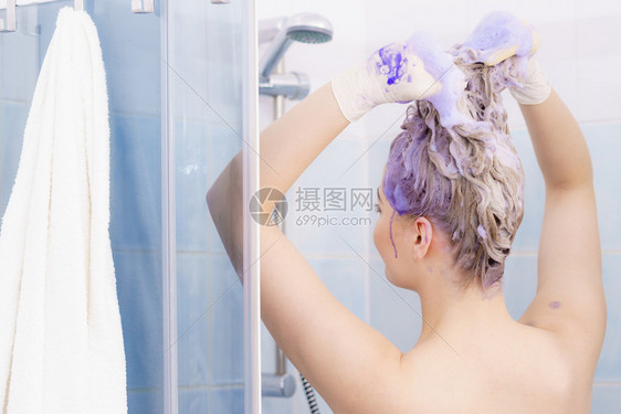 在金发上涂紫色墨粉洗发水时戴乳胶保护手套的妇女图片