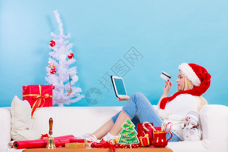 网上购物在互联网概念上购买圣诞礼物坐在沙发上持有平板和信用卡的圣诞妇女浏览网在上购买圣诞礼物的妇女在网上购买圣诞礼物的妇女图片