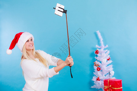 现代假日概念穿着圣诞礼帽的金发女人给自己拍圣诞照手持智能机的自拍图片